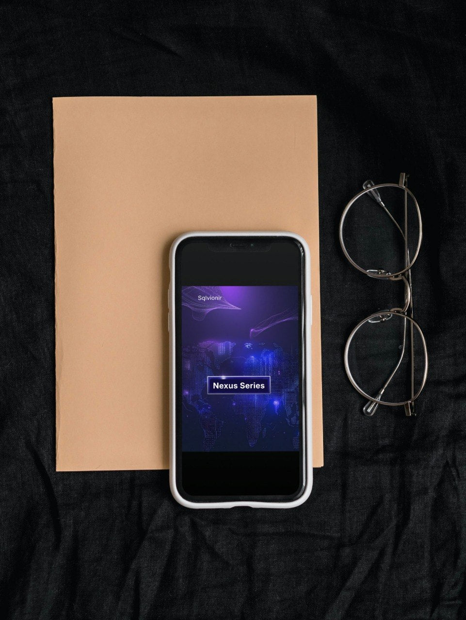 Smartphone with app interface on a brown paper sheet, next to eyeglasses on a dark fabric background